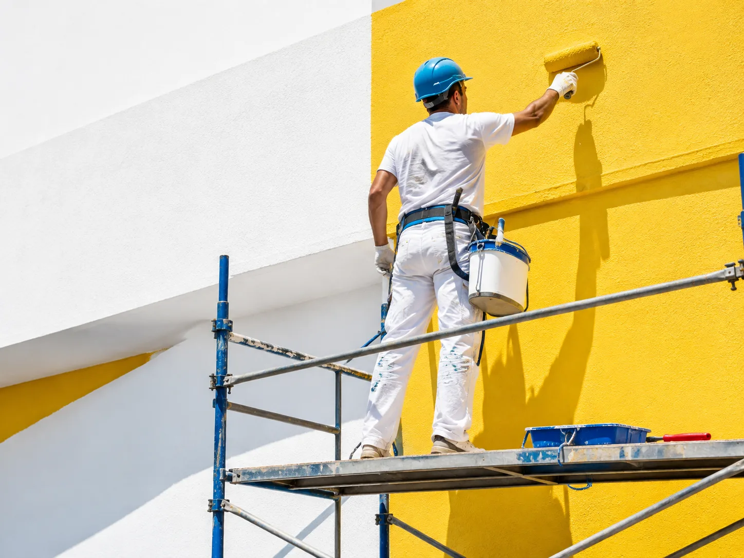 Pintor con casco trabajando sobre andamio en una fachada amarilla