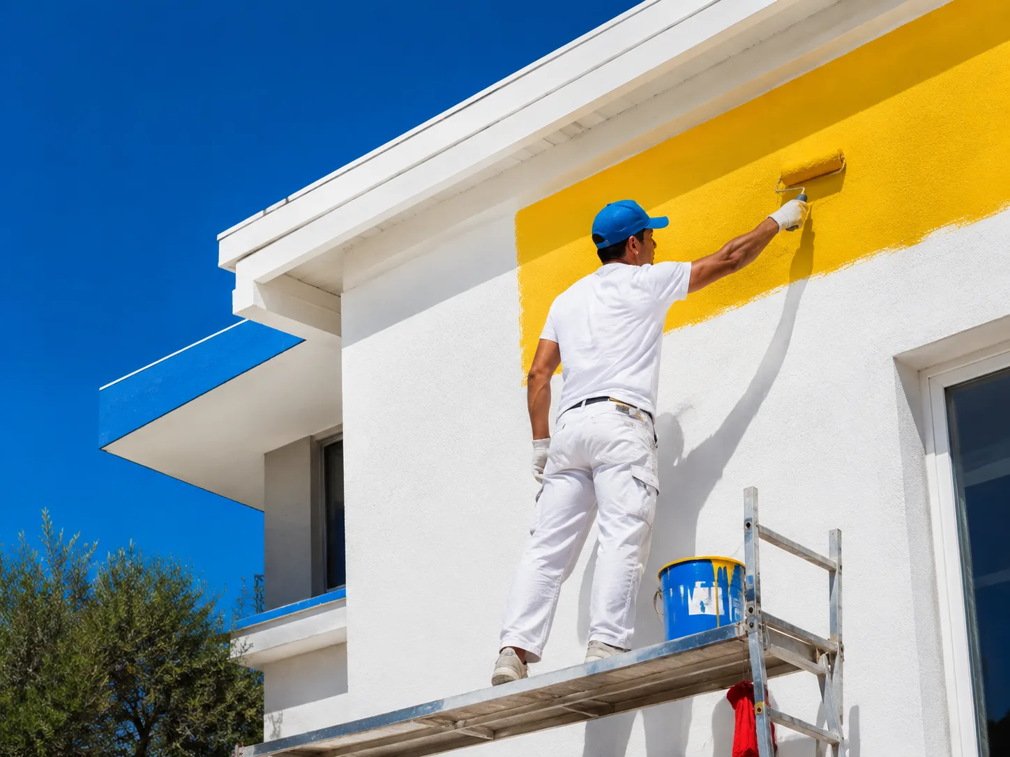 Pintor aplicando pintura amarilla en el exterior blanco de una vivienda
